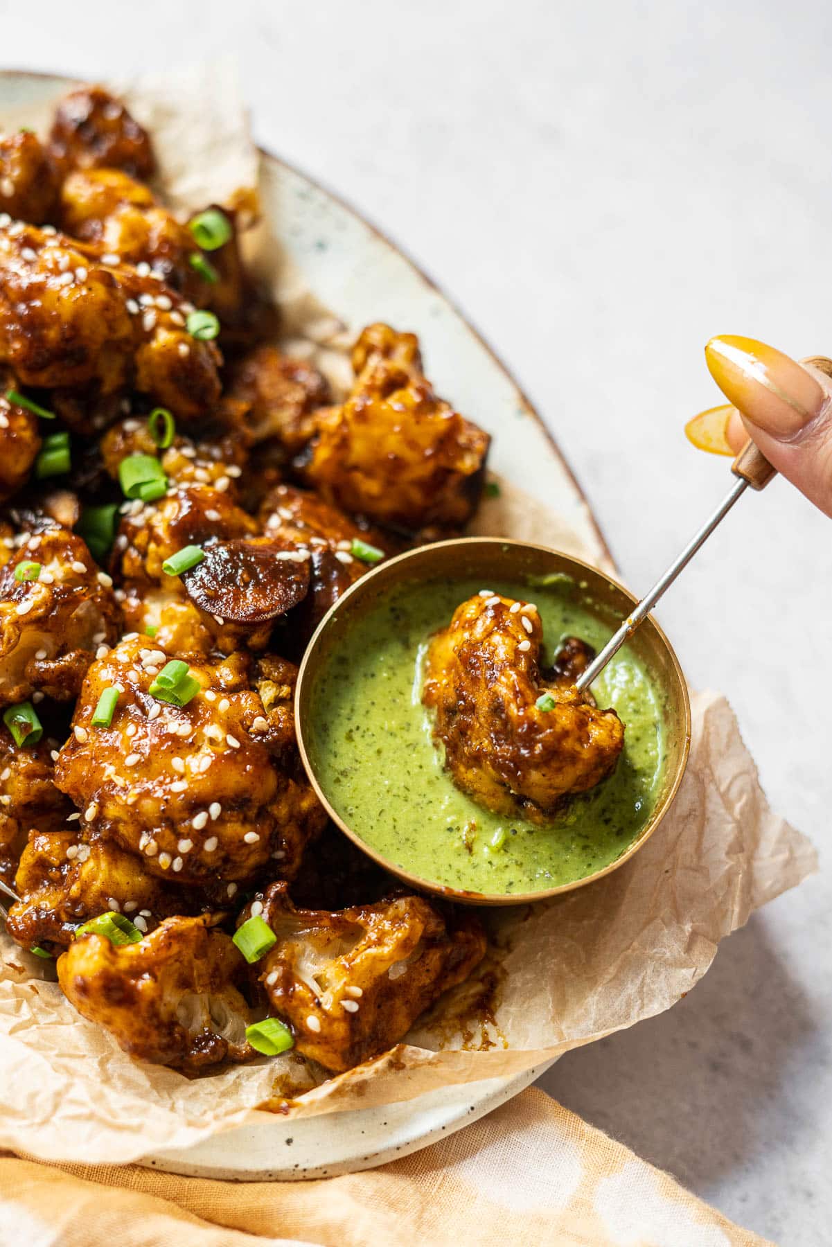 dipping a piece of mango-tamarind cauliflower wings in a condiment bowl of cilantro-mint chutney
