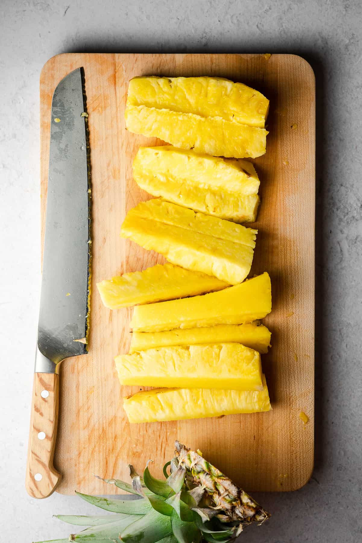 pineapple cut into spears on a cutting board with a bread knife with the pineapple stem