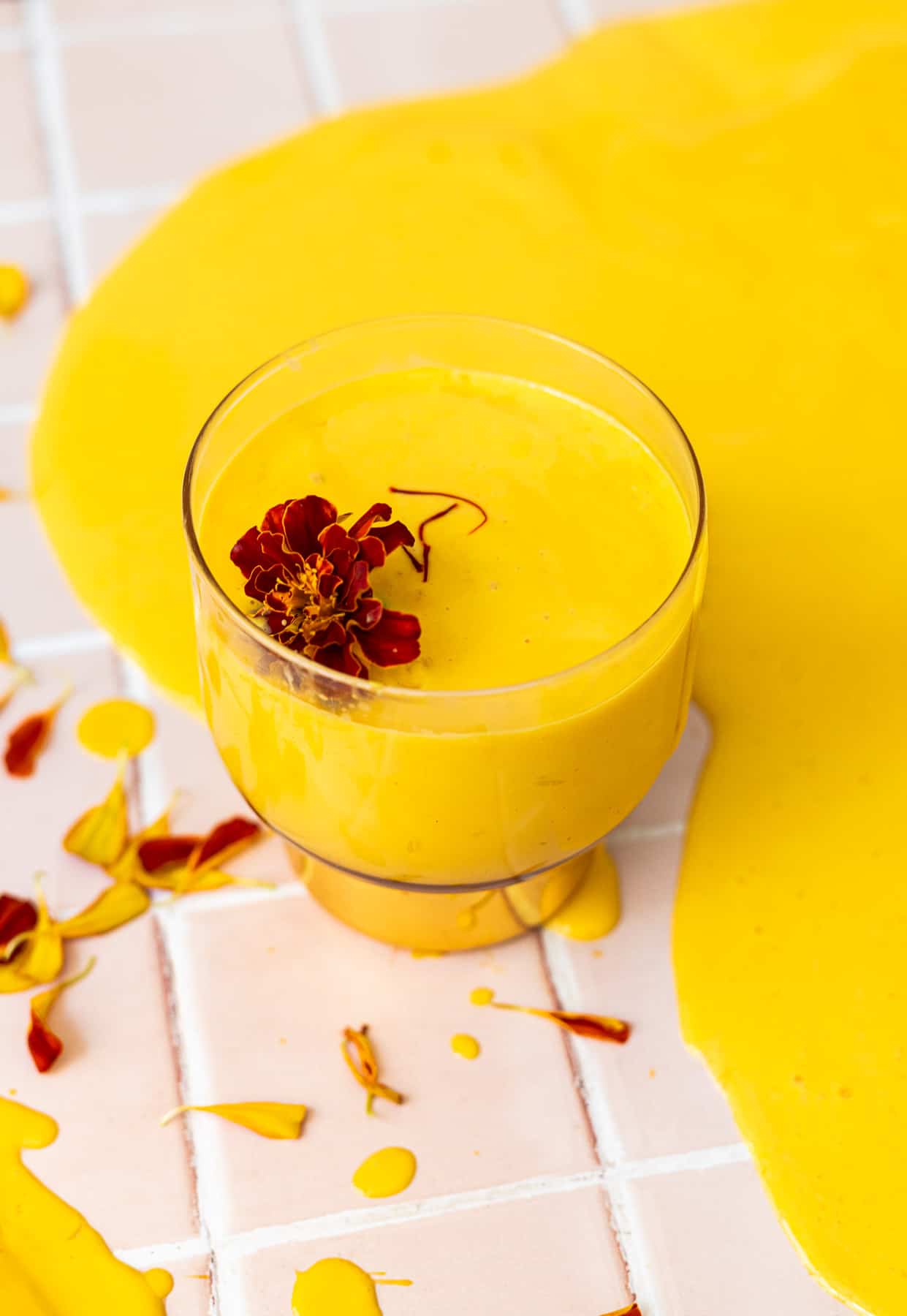 Mango lassi in an old fashioned glass with a large spill surrounding it with edible flowers and saffron