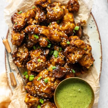 cauliflower wings in a platter with appetizer picks and a condiment bowl of mint-cilantro chutney and fresh tamarind.