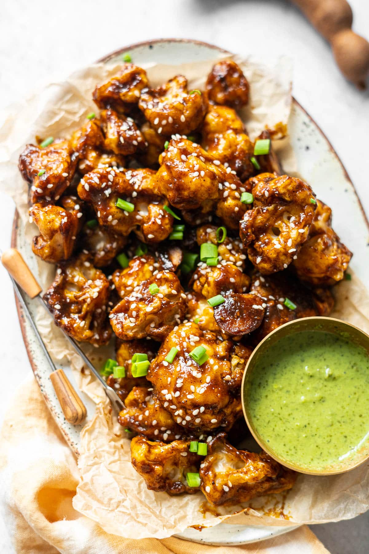 Close up Back Lit photo of cauliflower wings in a platter with appetizer picks and a condiment bowl of mint-cilantro chutney.