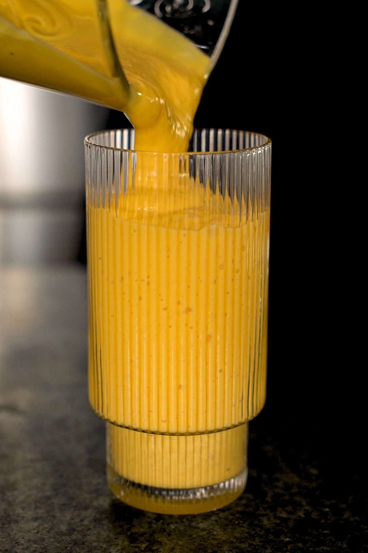 pouring a mango lassi out of a blender into a tall glass