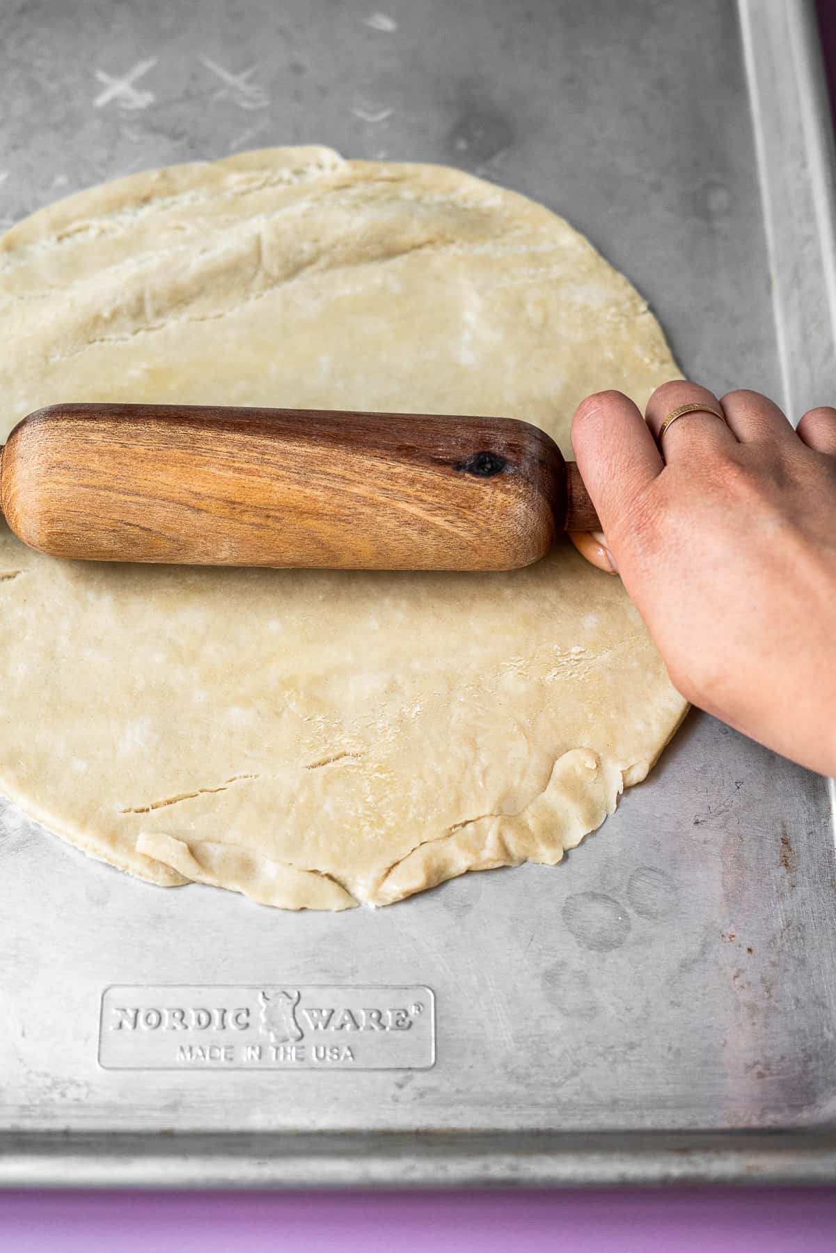 using a rolling pin to roll out a circular premade pie crust in a sheet tray