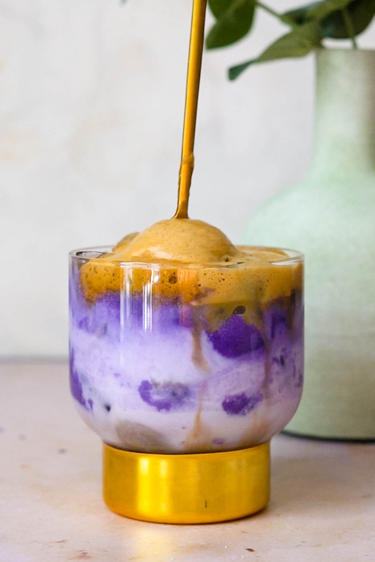 a gold spoon stirring instant espresso with ube and coconut milk