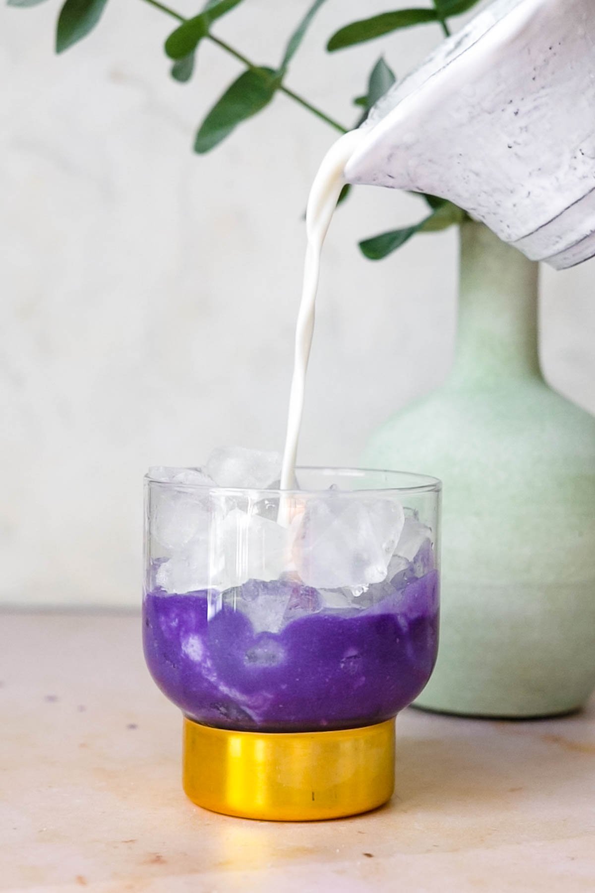Pour Milk from a white pourer into a highball glass with ube and coconut milk filled with ice