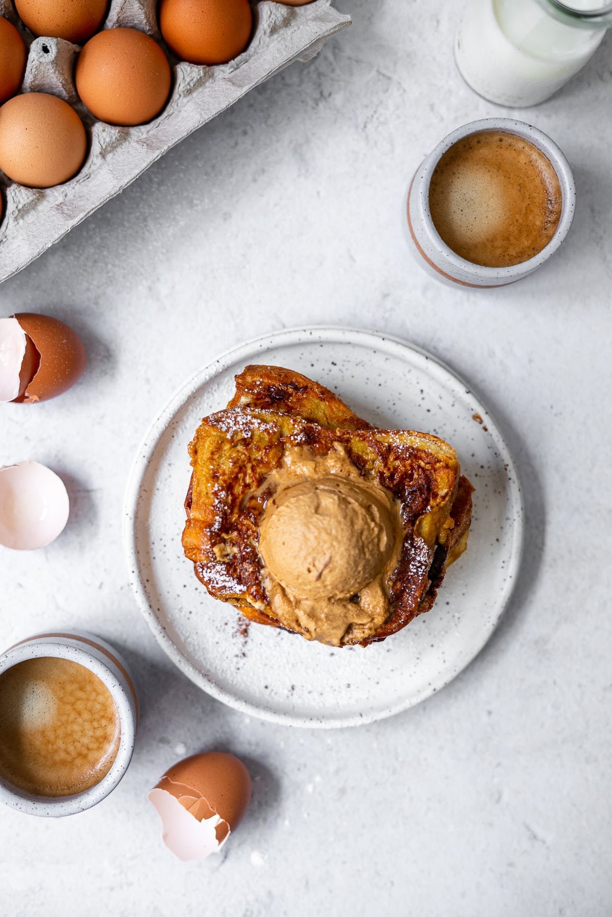 flatlay of french toast, espresso, cracked eggs, eggs in a carton, and milk