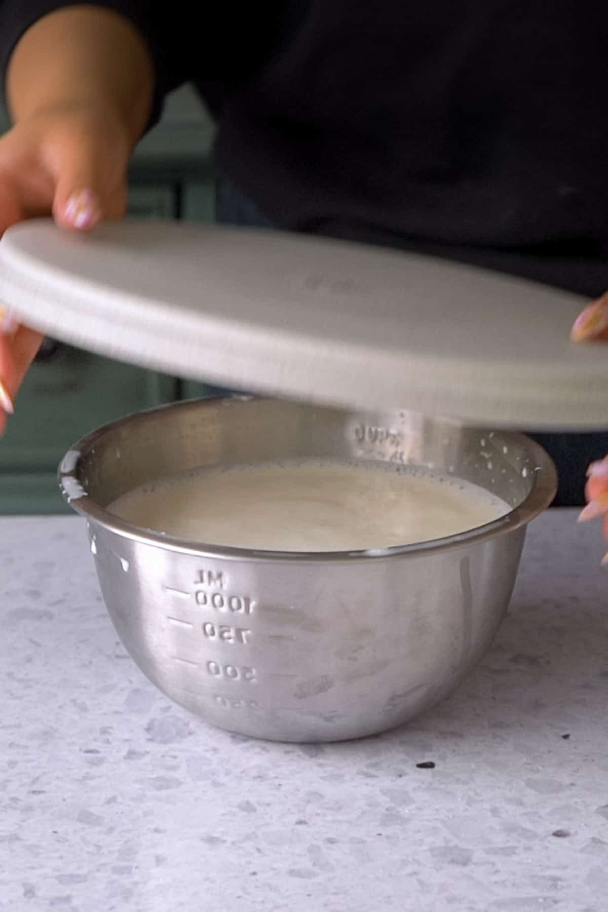 covering the boiled frothed milk in a metal bowl with a plate