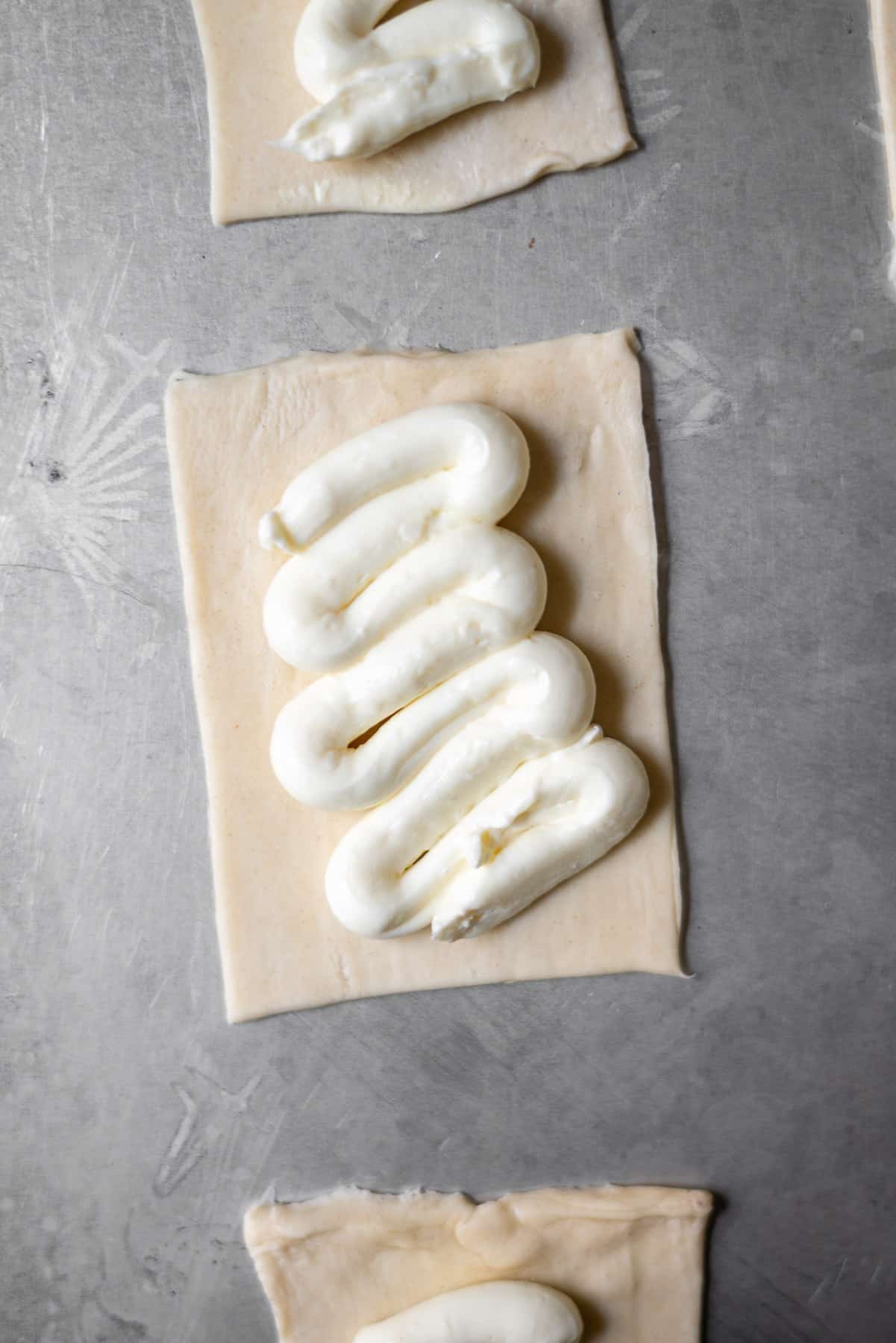 cream cheese piped in a snake motion on a puff pastry rectangle on a metal sheet