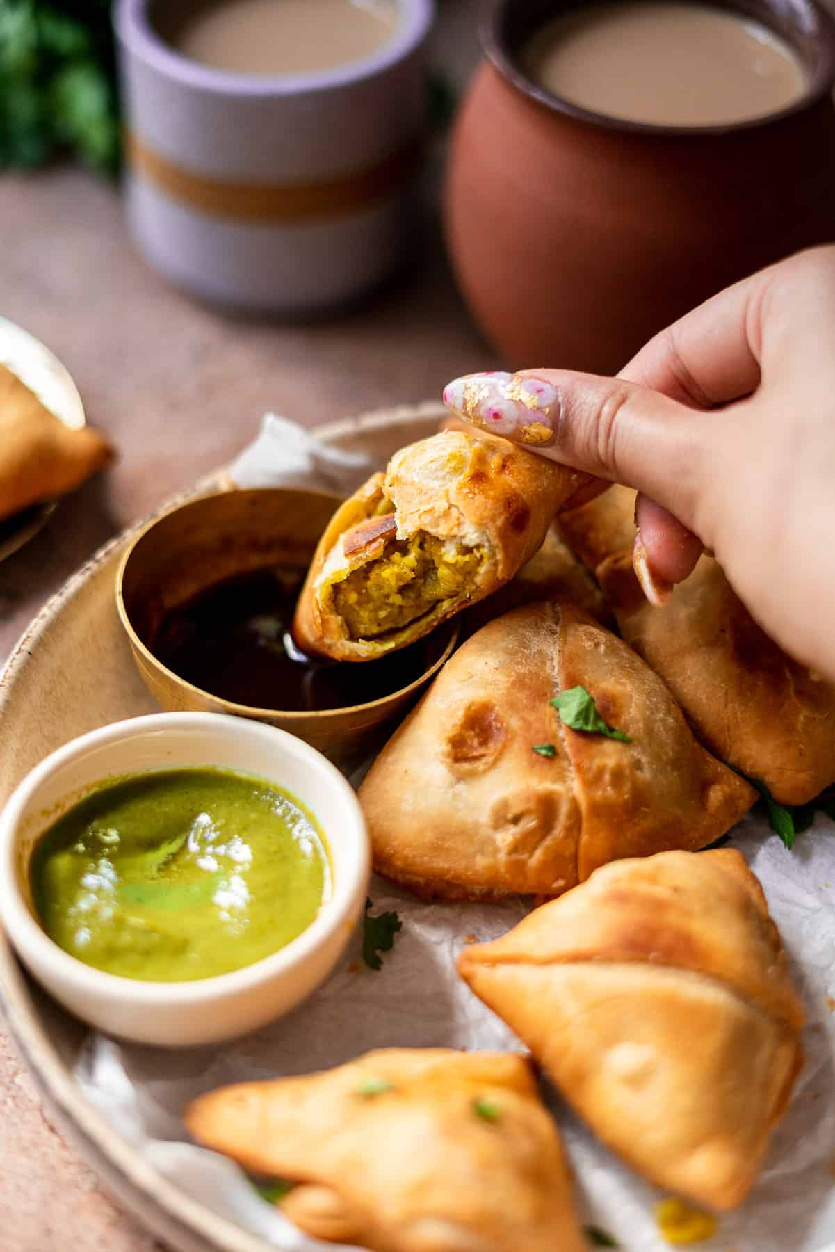 dipping a samosa in imli chutney with chai in the background