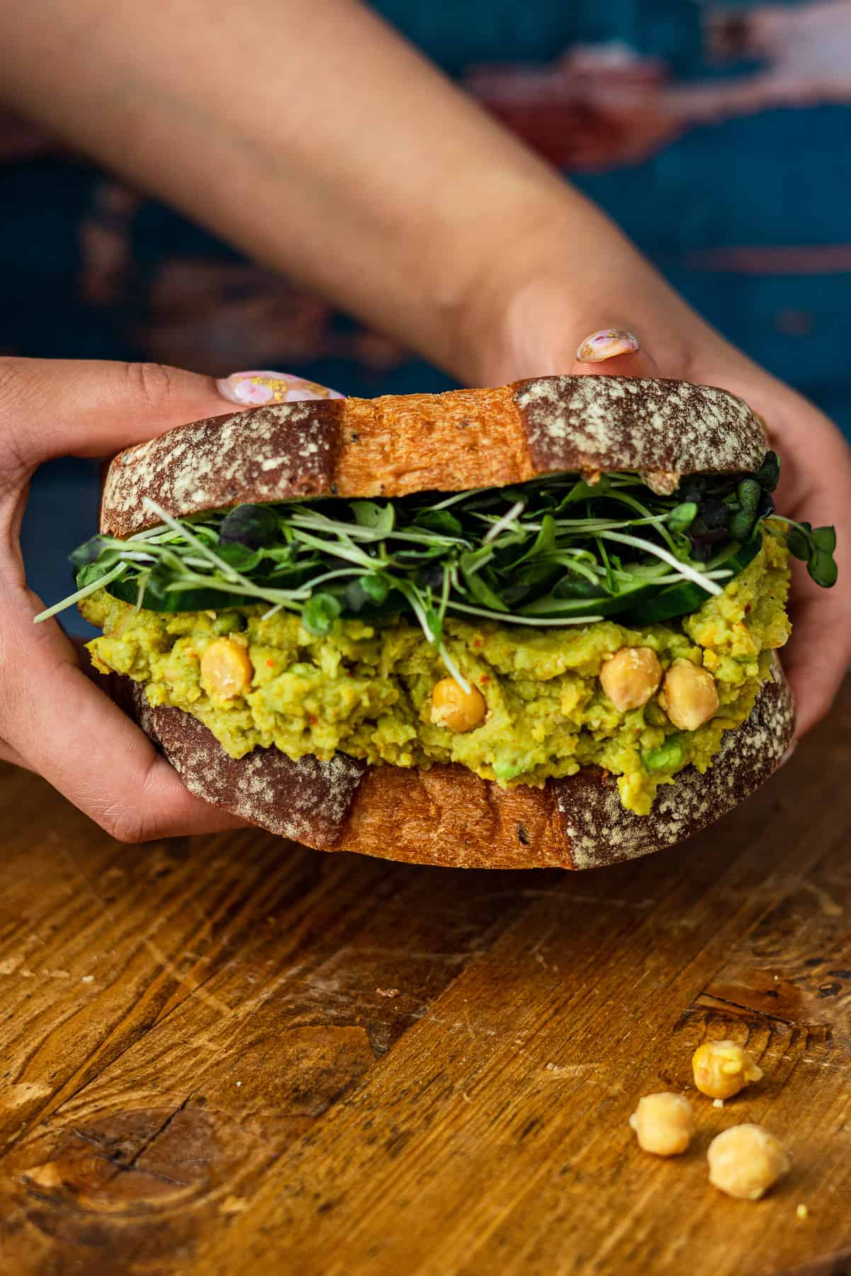 two hands Grabbing Smashed Avocado and Chickpea Sandwich