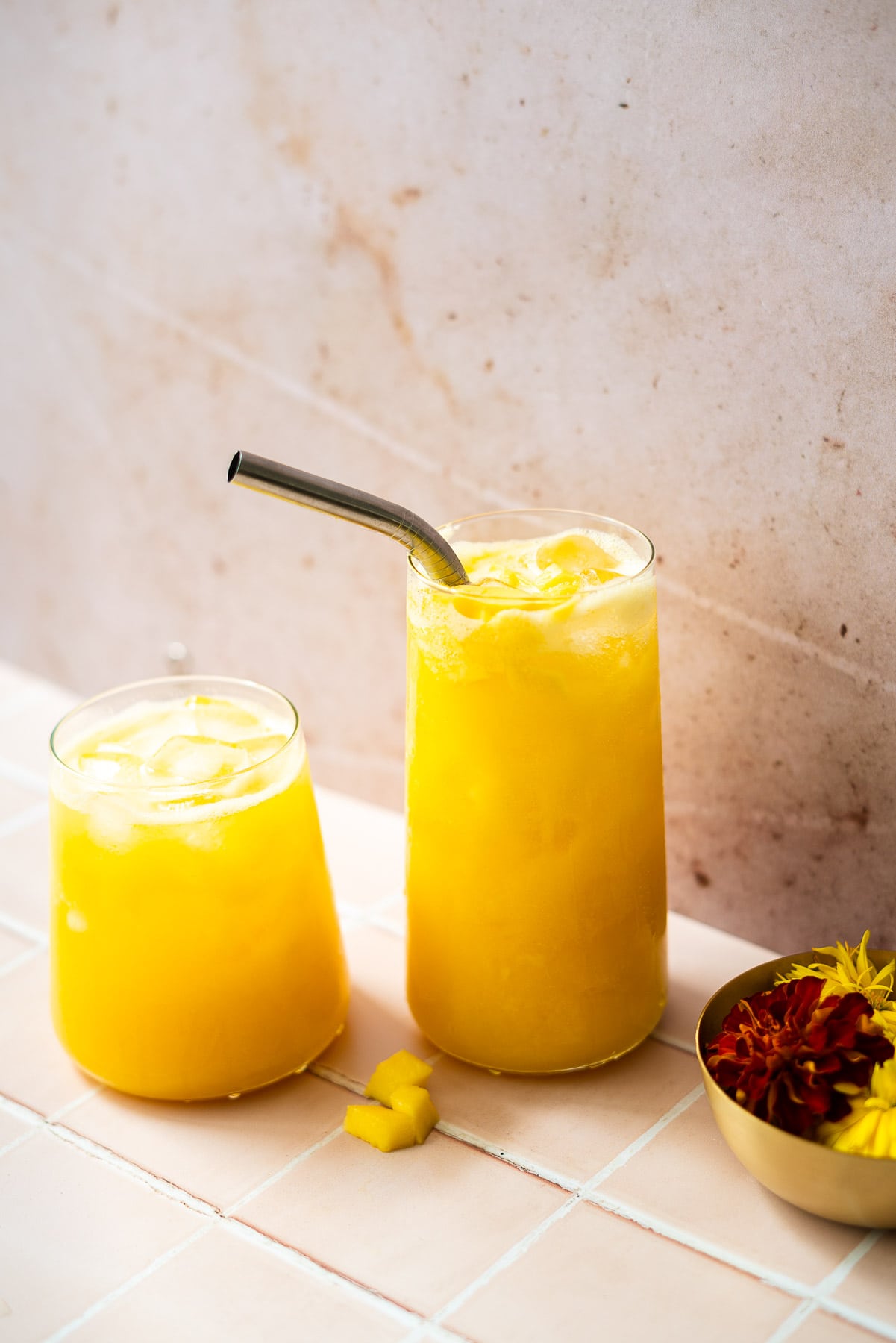 two glasses filled with mango juice with a metal straw and mango chunks
