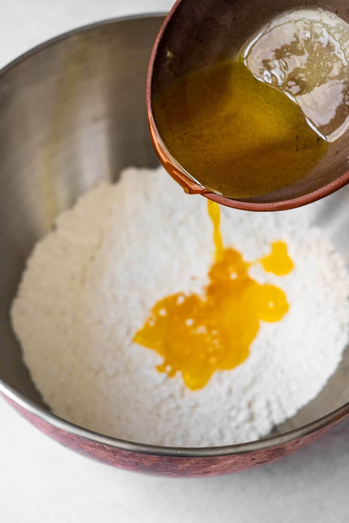 pouring ghee into flour into a mixing bowl