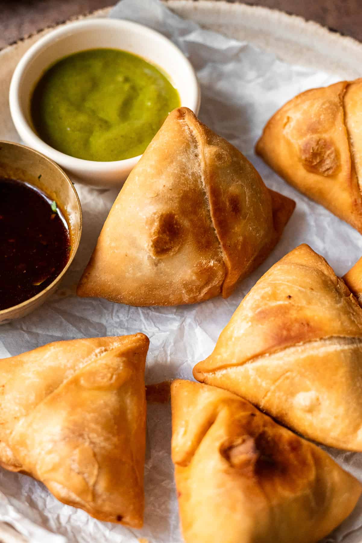 samosa in a plate propped up against chutneys