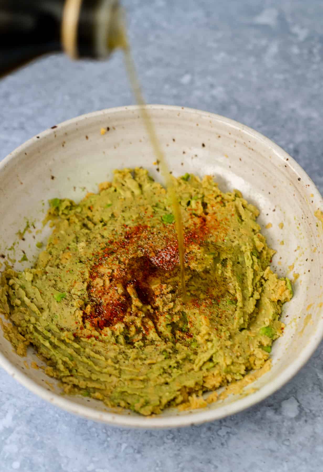 pouring olive oil into smashed chickpeas and avocado salad with spices