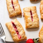 strawberry and cream cheese turnovers on a white board with fresh strawberries and a fork