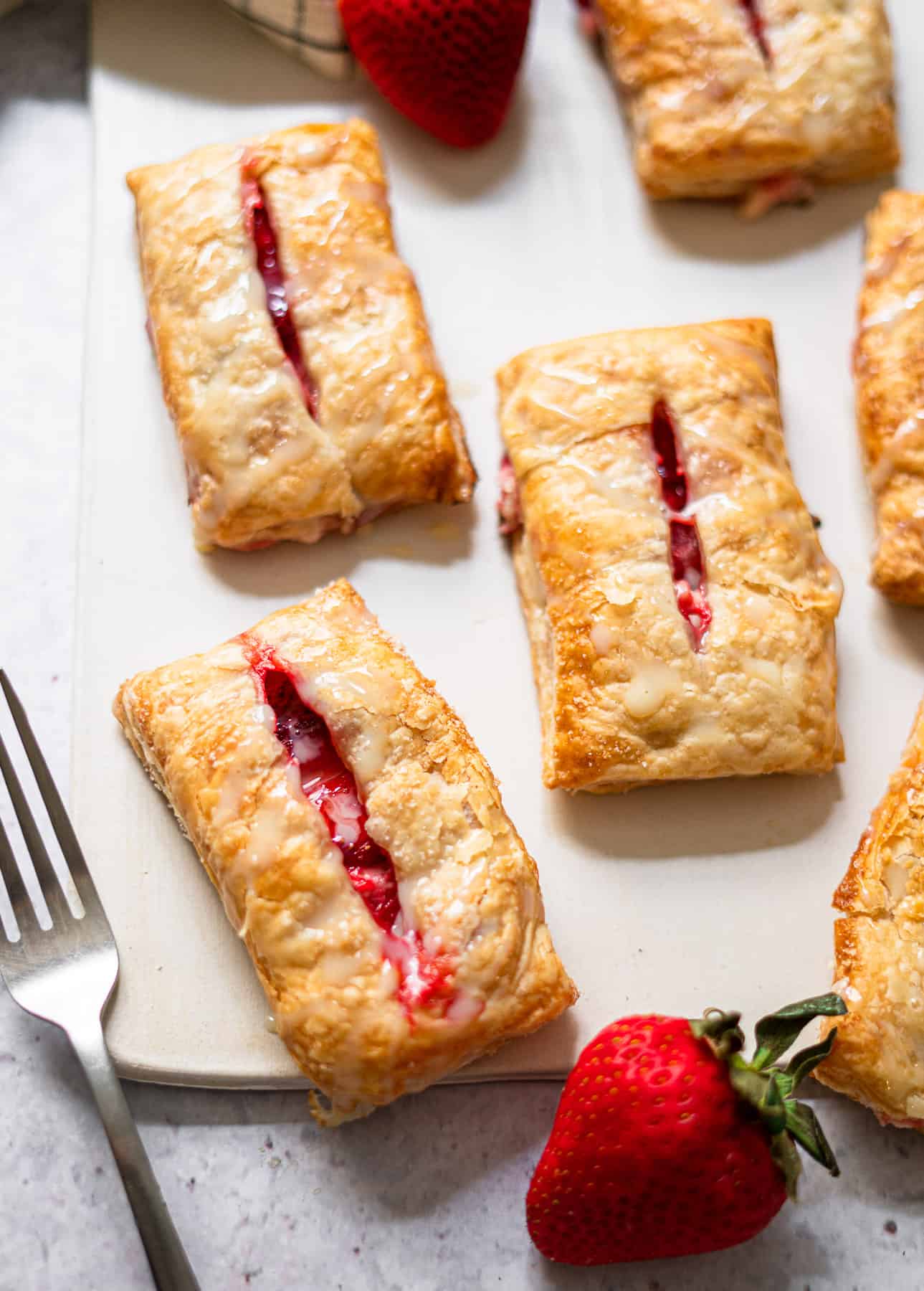 strawberry and cream cheese turnovers on a white board with fresh strawberries and a fork