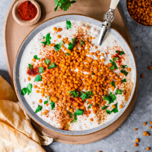 Boondi Raita in a big bowl with a serving spoon on a platter with chili powder, cilantro, and boondi