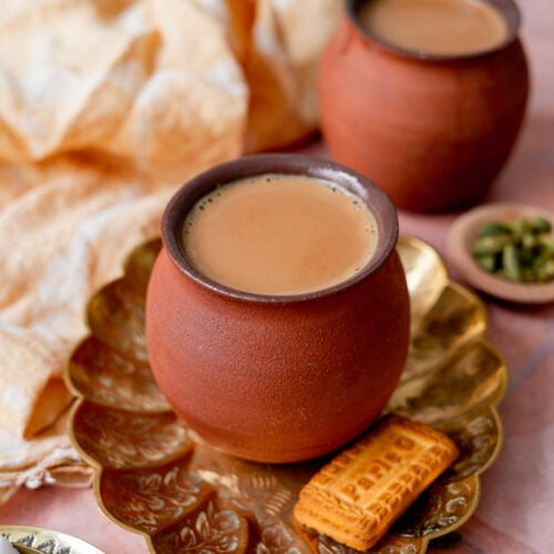 masala chai cups in a platter with sugar, parle g, and cardamom