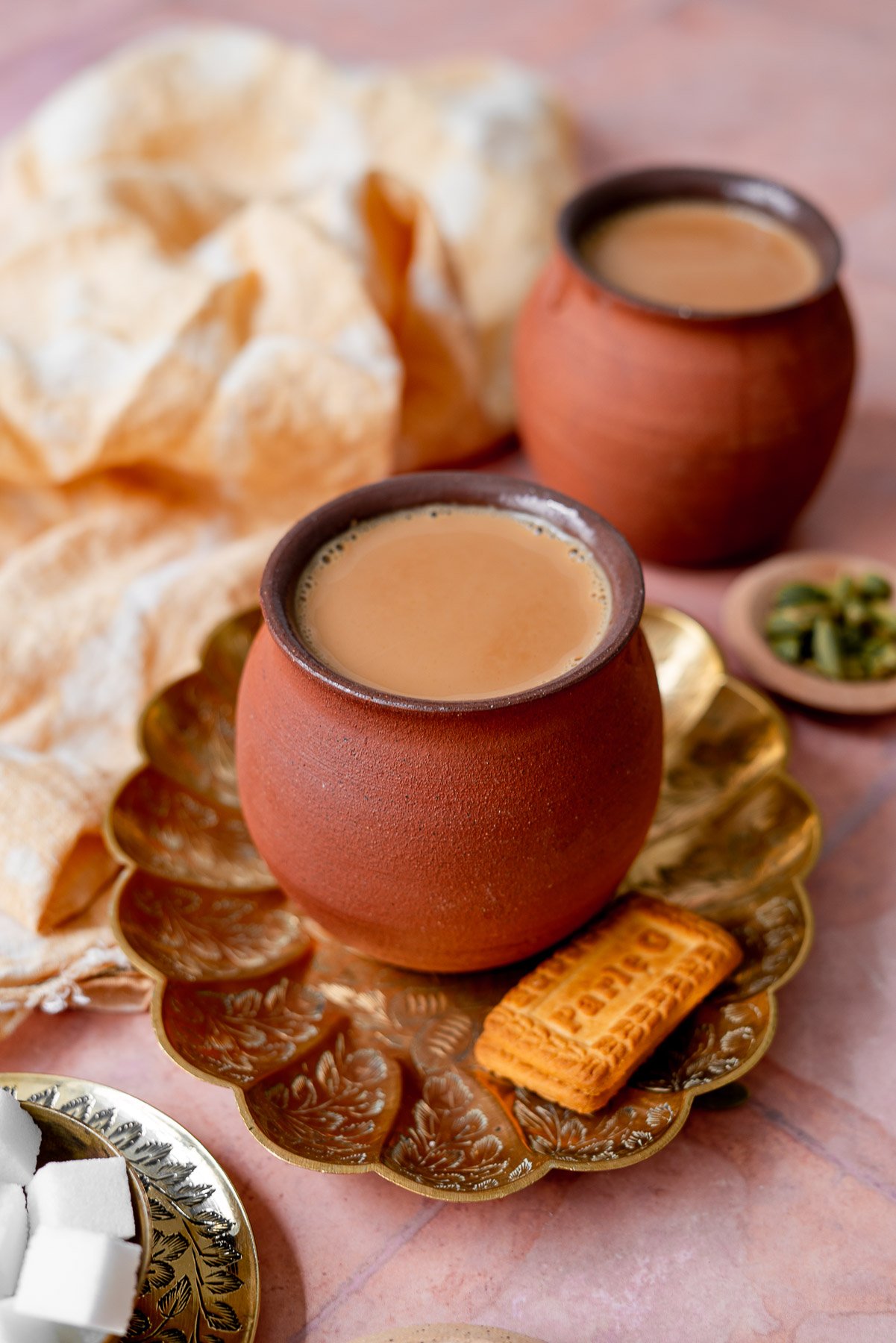 masala chai cups in a platter with sugar, parle g, and cardamom