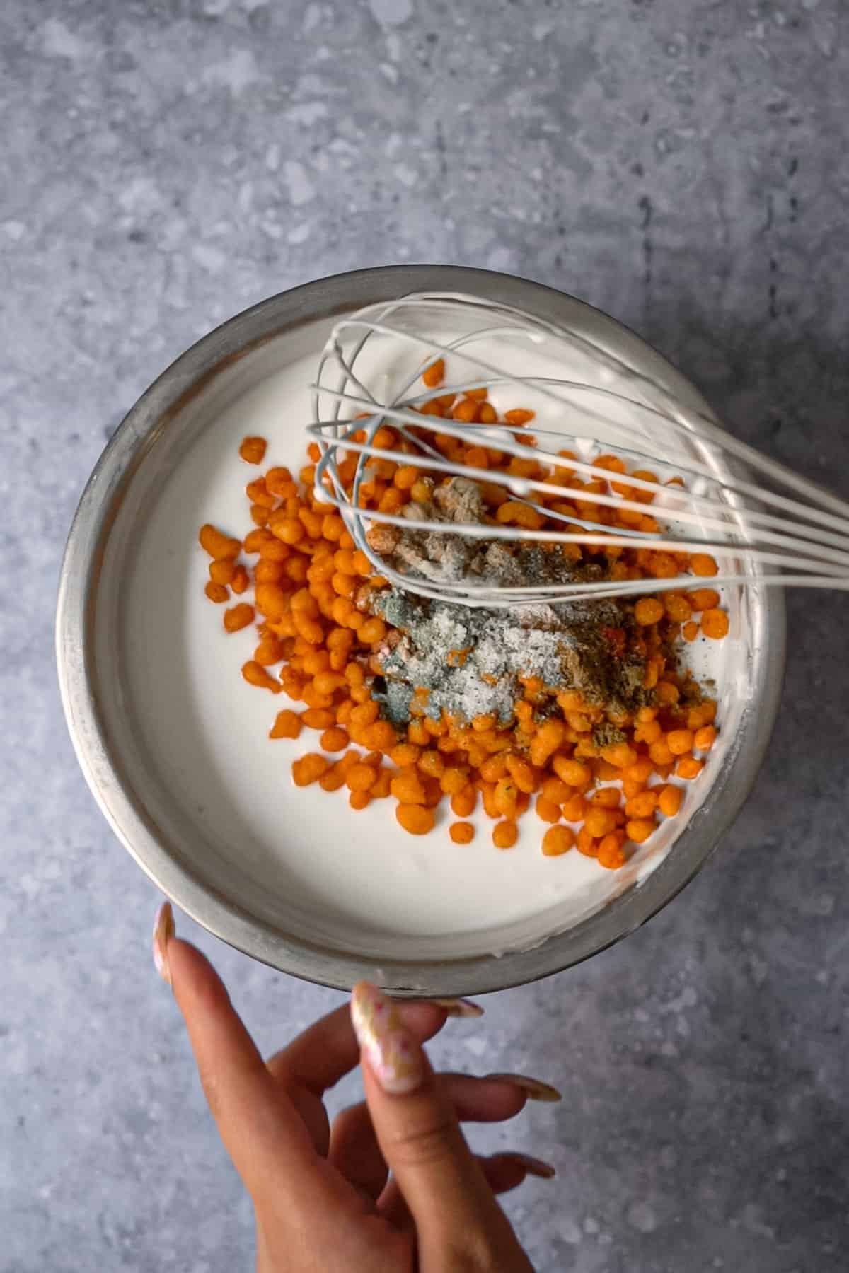 Mixing boondi raita together in a bowl with a whisk