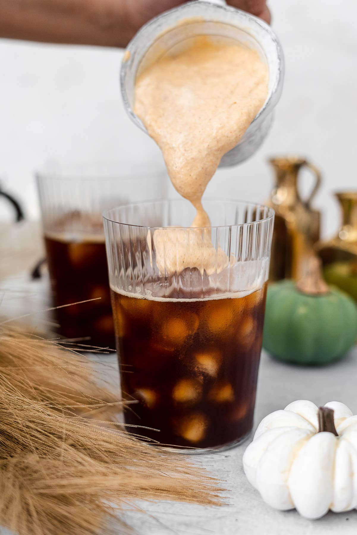 pouring pumpkin cream cold foam from a pourer into a cup of coffee