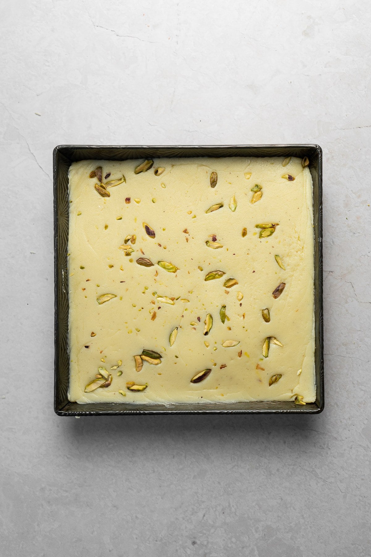 white barfi with chopped pistachios setting in square pan