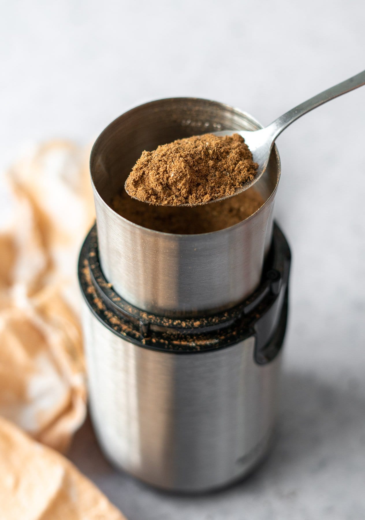 a spoon lifting chai masala out of a spice grinder
