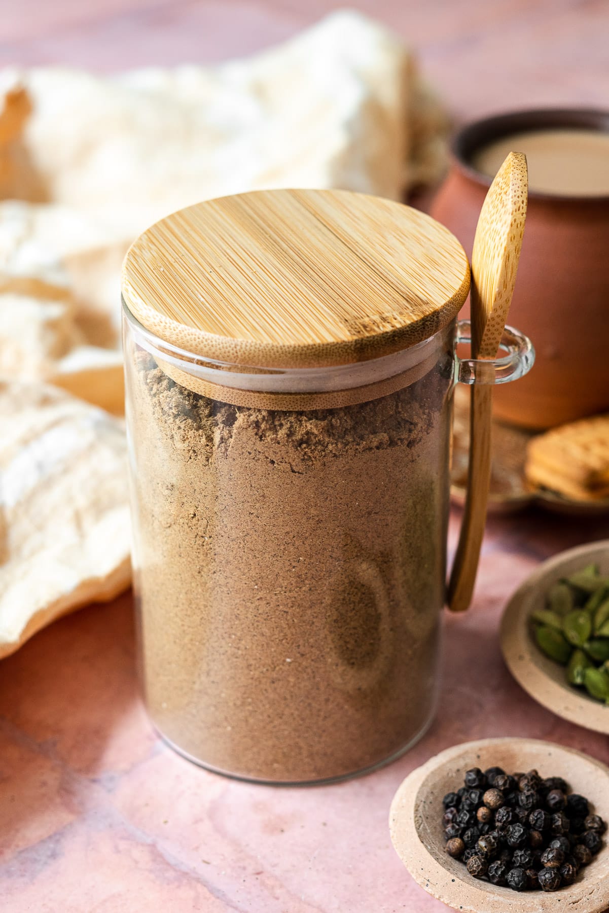 chai masala in a container with black pepper and cardamom seeds