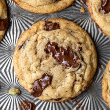 a single chai spice chocolate chip cookie with smears of chocolate and several cookies surrounding it