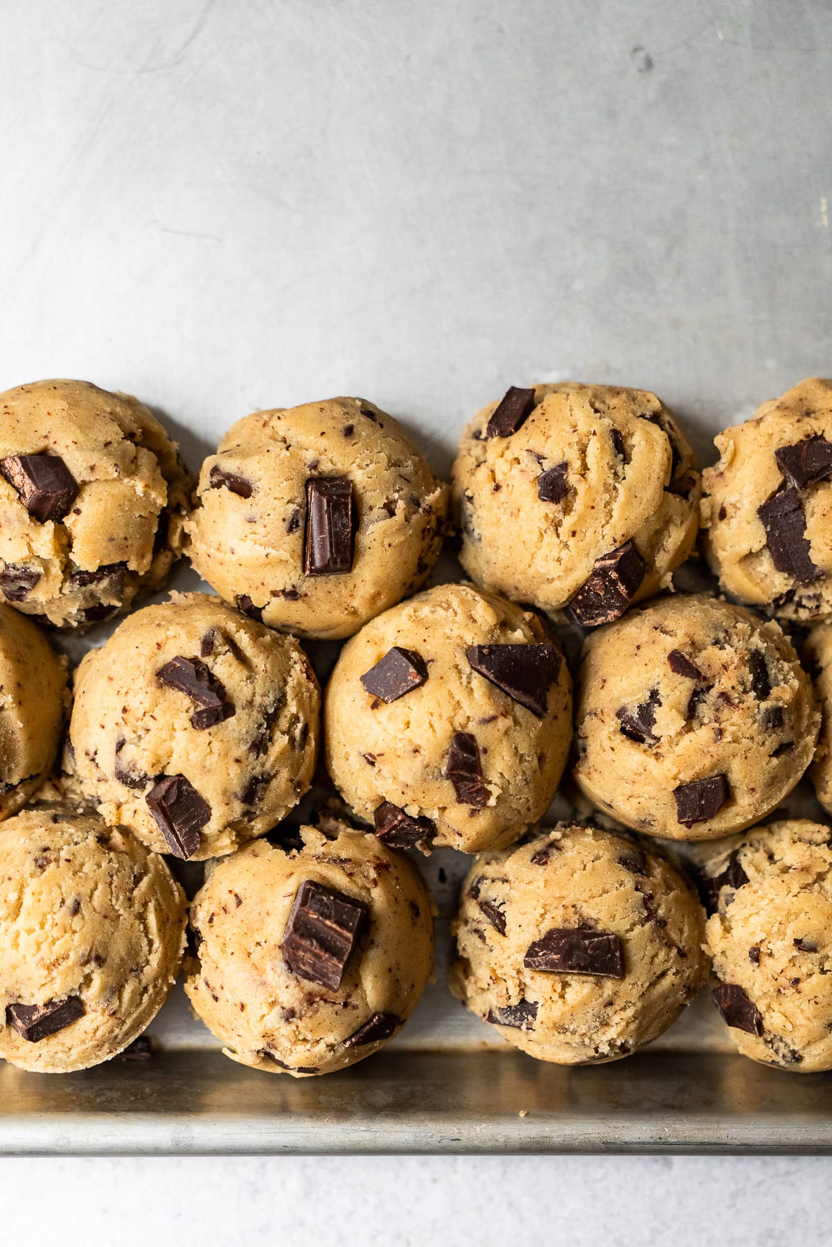 balls of chocolate chunk cookie dough in three rows on a baking sheet