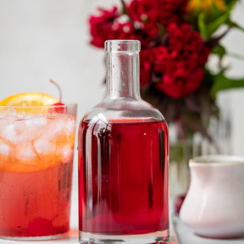 glass bottle with grenadine with a shirley temple and red flowers in the background