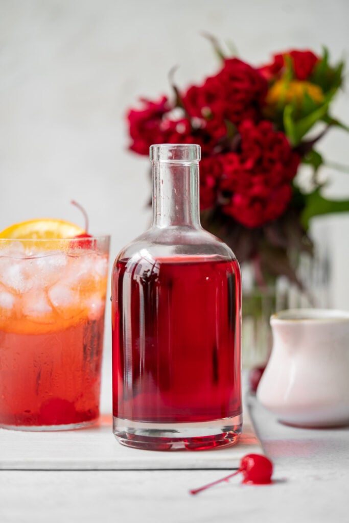 glass bottle with grenadine with a shirley temple and red flowers in the background