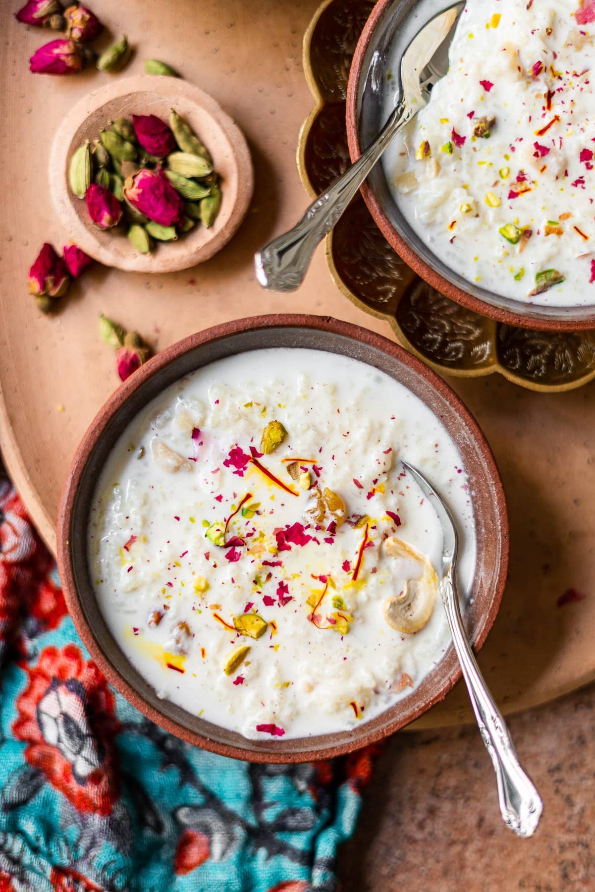 bowl of kheer with spoon on a platter with cardamom and roses