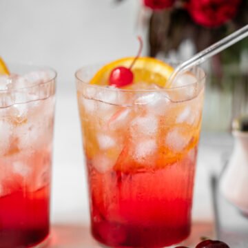 two glasses of shirley temple side by side with fresh cherries