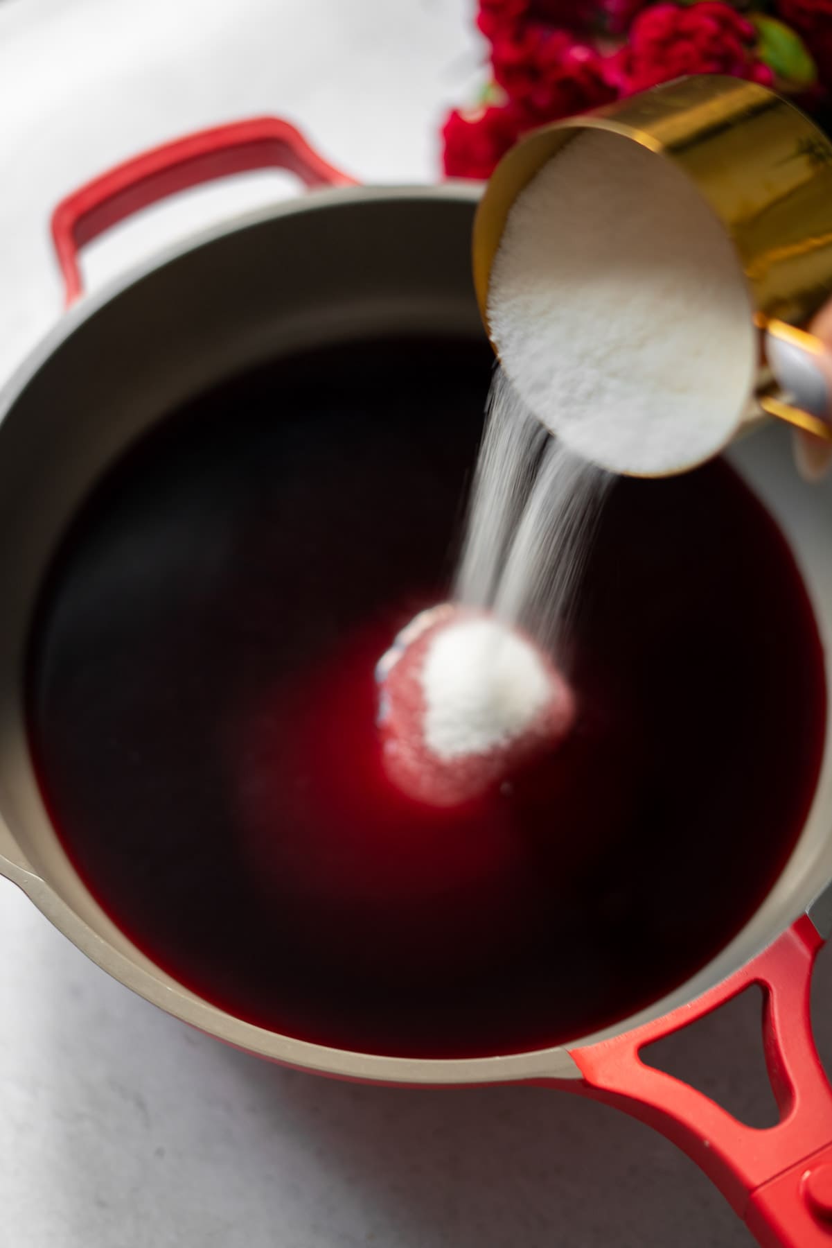 pouring sugar into a red pan with pomegranate juice