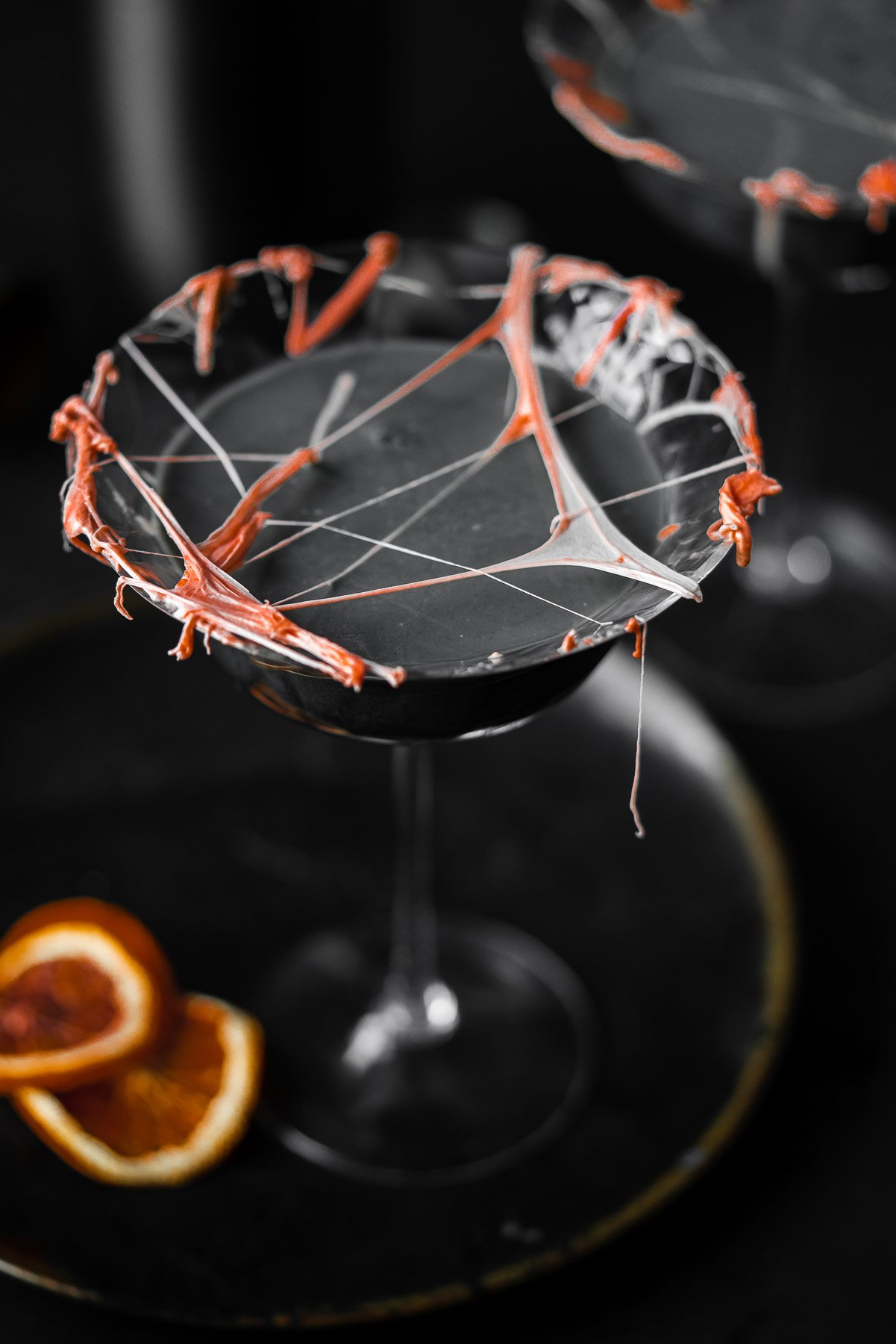 a coupe glass filled with a cocktail with marshmallow cob webs and dried blood oranges