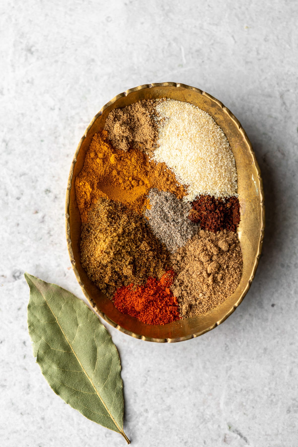 several different spices in a bronze tray with a bay leaf