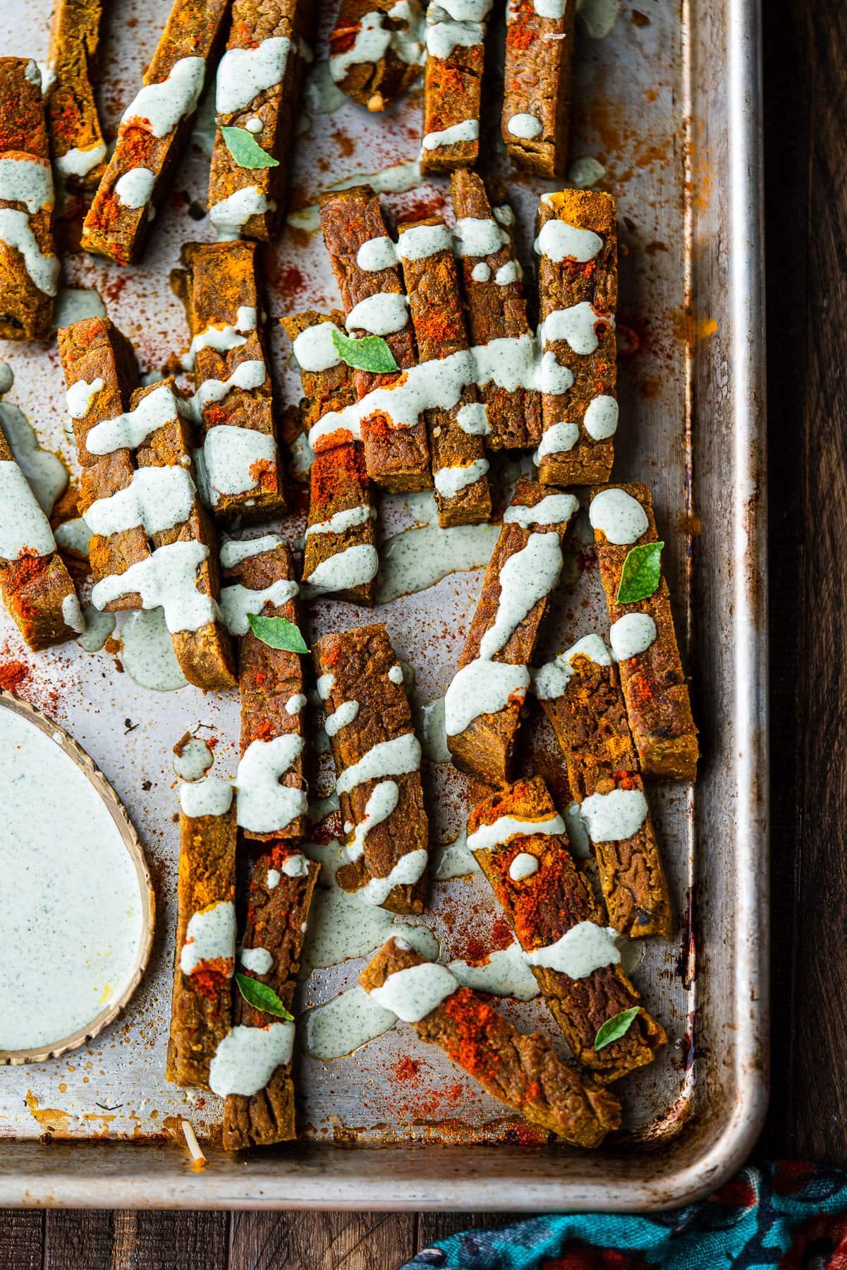 a tray full of chickpea fries garnished with curry leaf ranch on a wooden surface