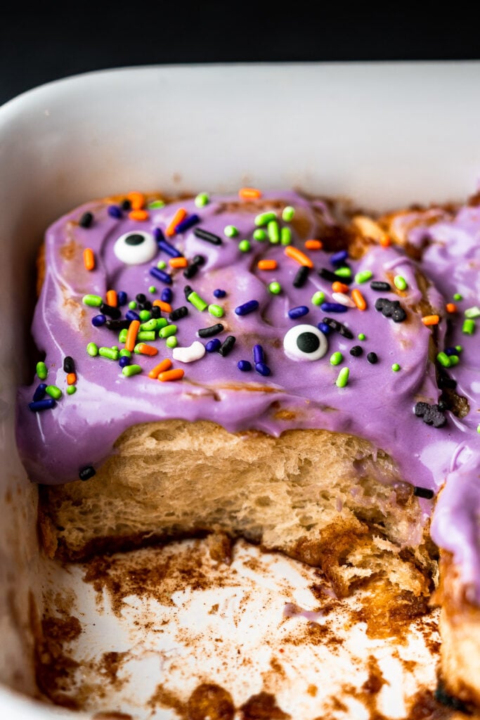 one cereal milk cinnamon roll in a baking dish with halloween sprinkles