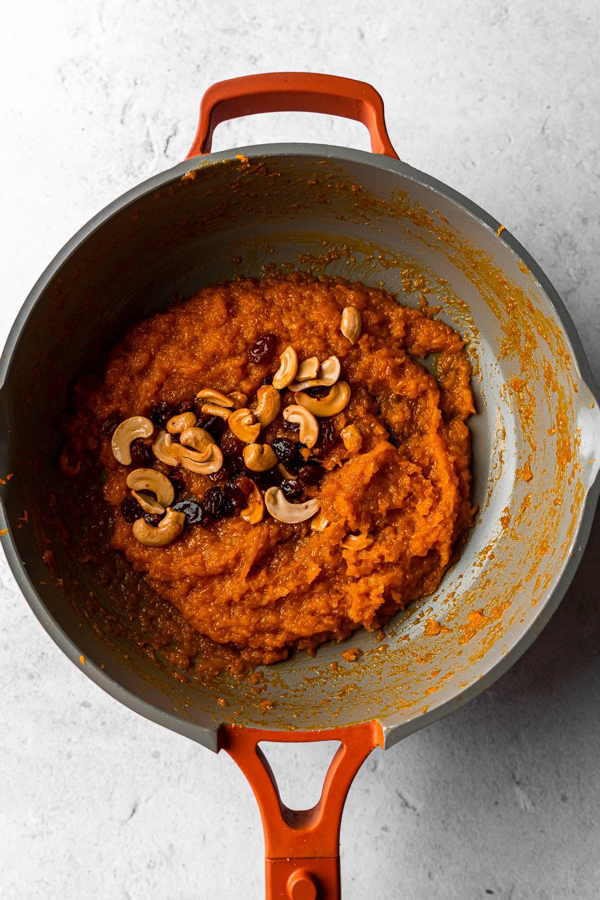 cooked pumpkin halwa in a pan with toasted cashews and golden raisins