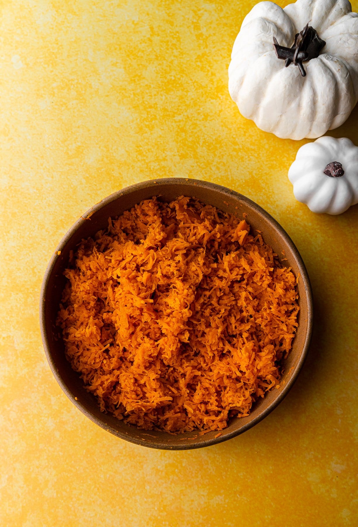 shredded white pumpkin in a bowl with two decorative pumpkins