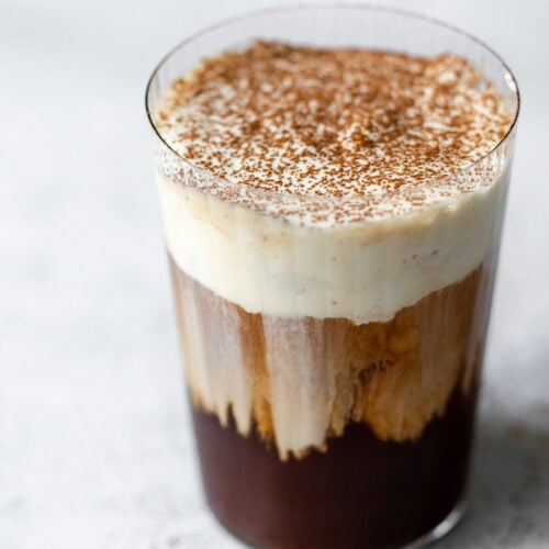 a glass filled with cold brew and sweet cream cold foam cascading down the glass topped with cocoa powder