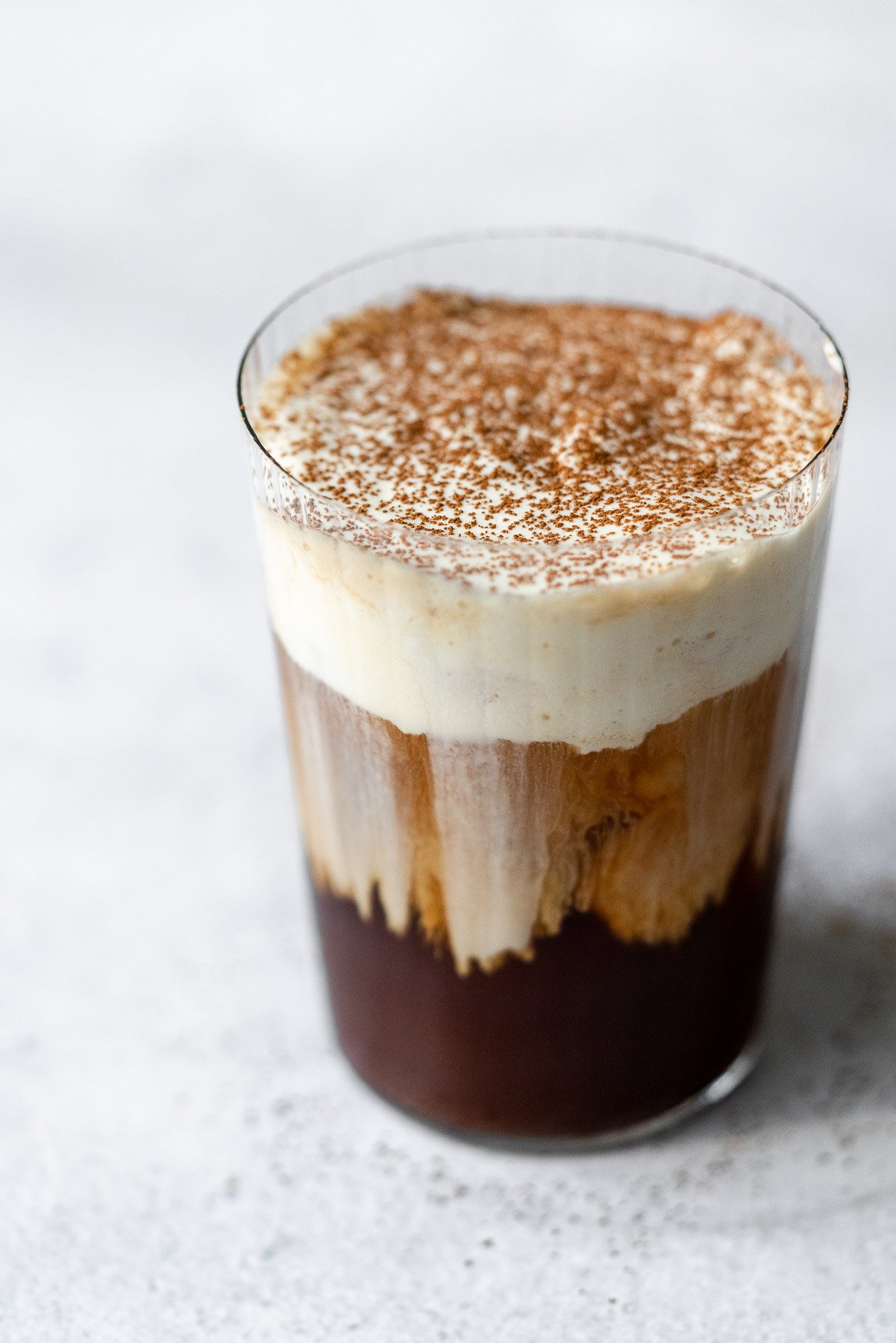 a glass filled with cold brew and sweet cream cold foam cascading down the glass topped with cocoa powder