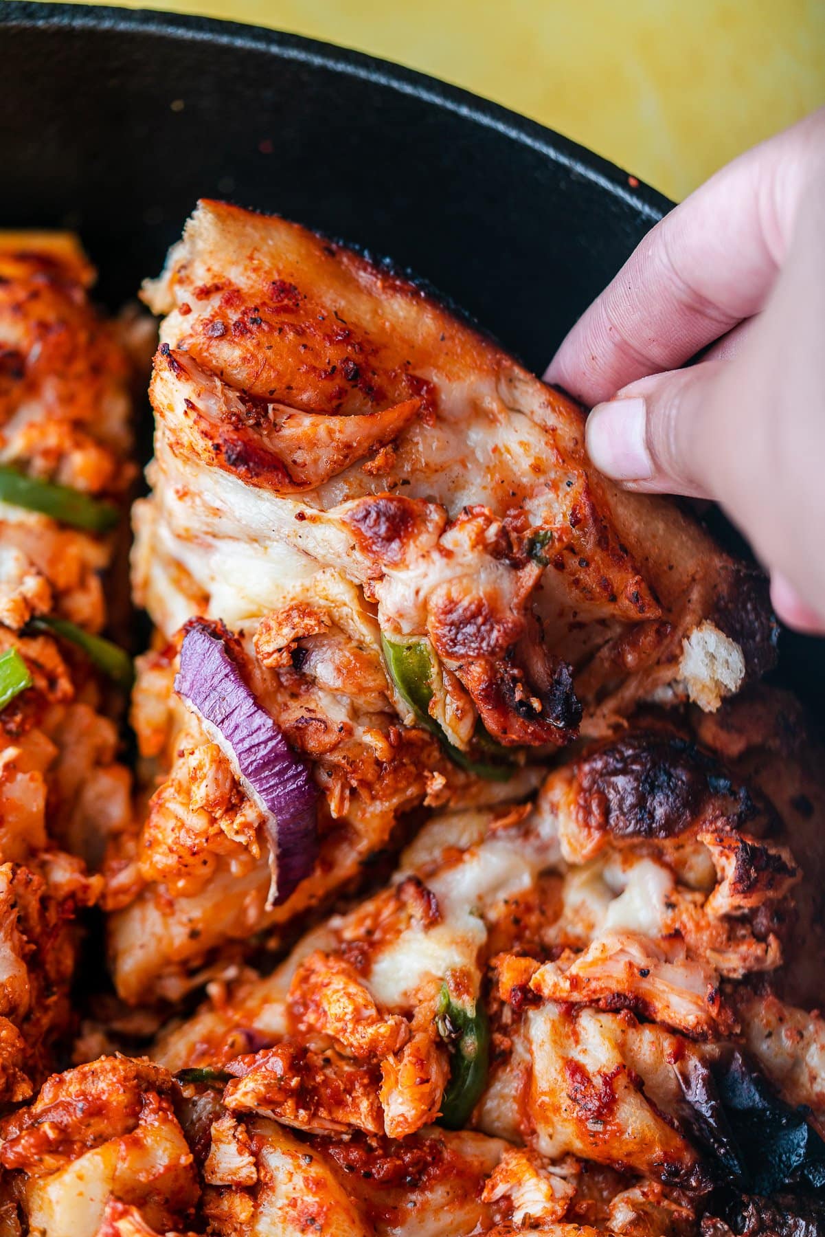 a hand grabbing a slice of tandoori chicken pizza from the skillet
