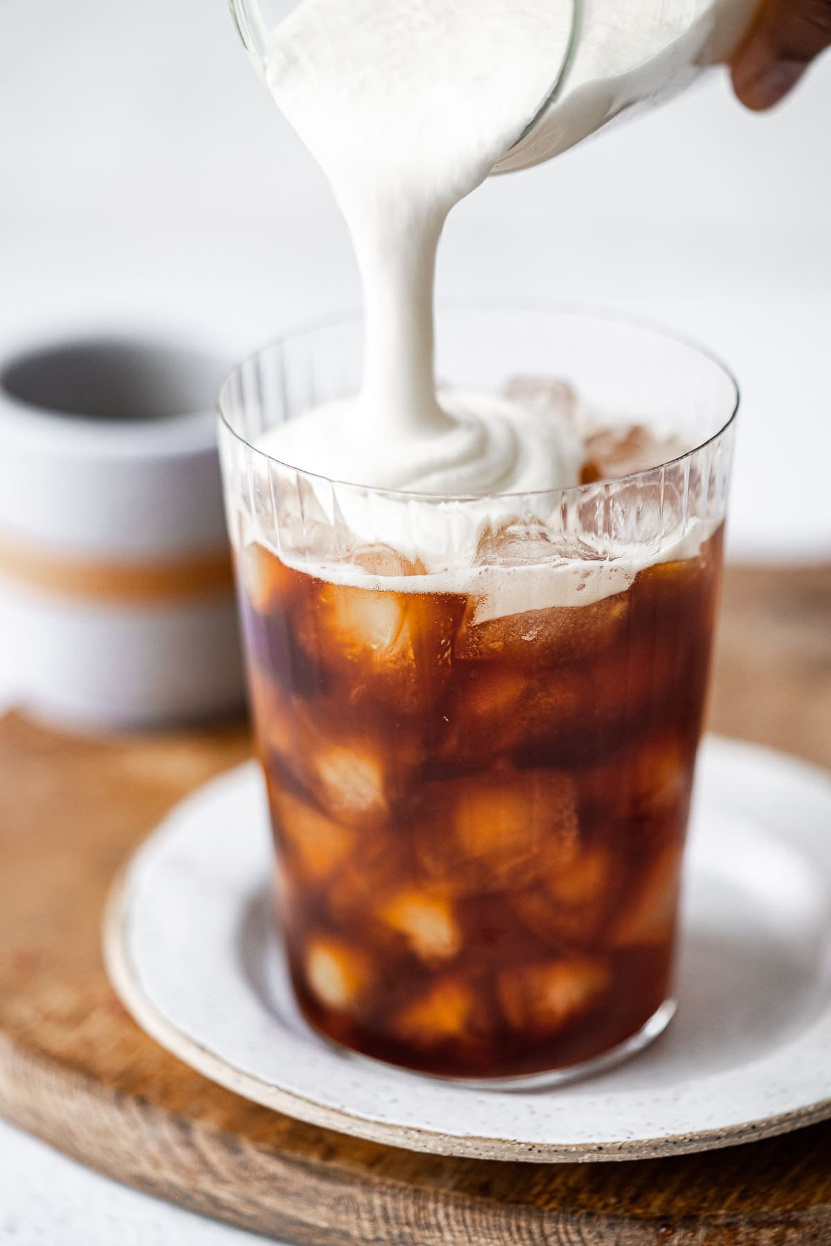 pouring sweet cream cold foam into a cup of iced coffee