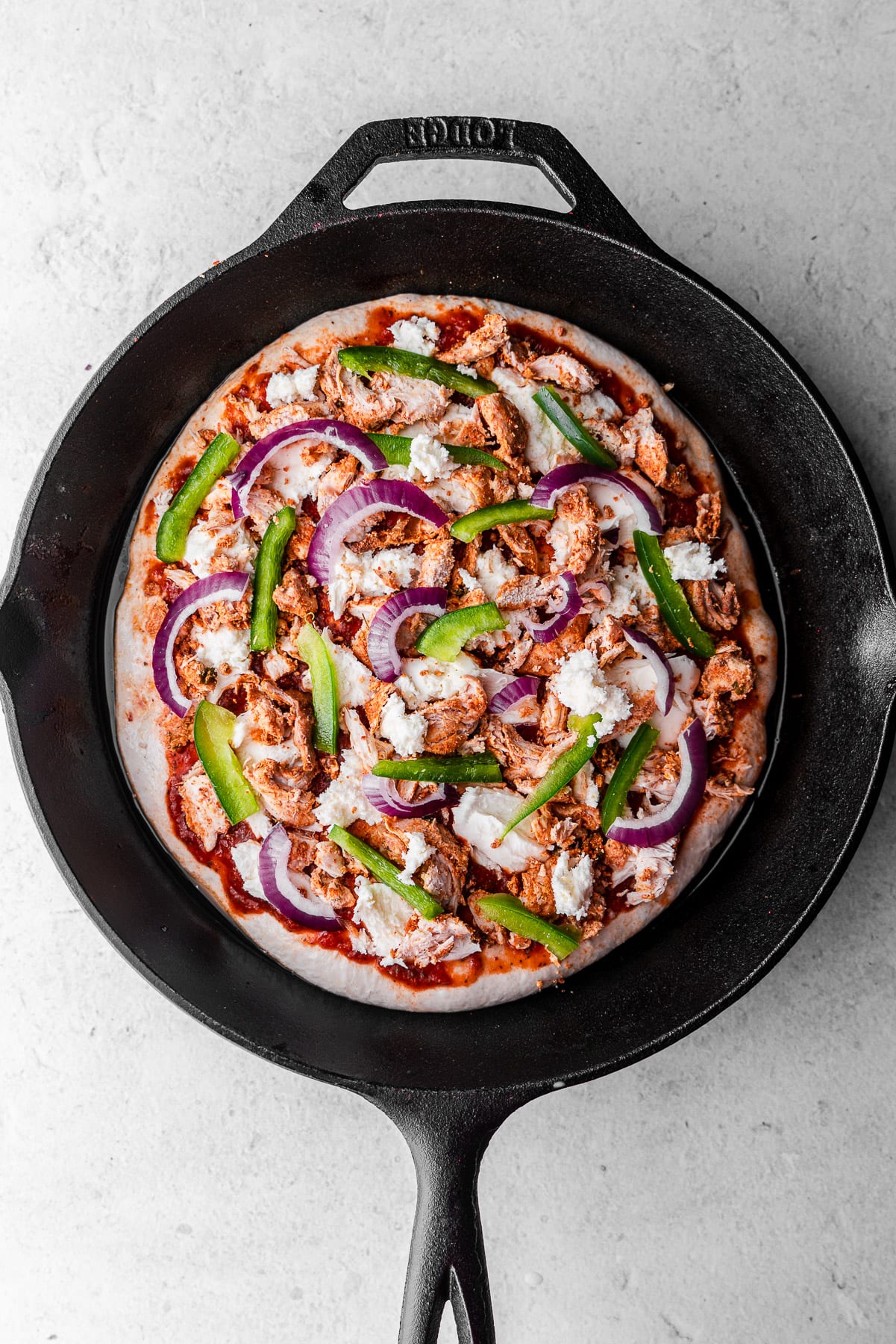 unbaked tandoori chicken pizza in a cast iron skillet