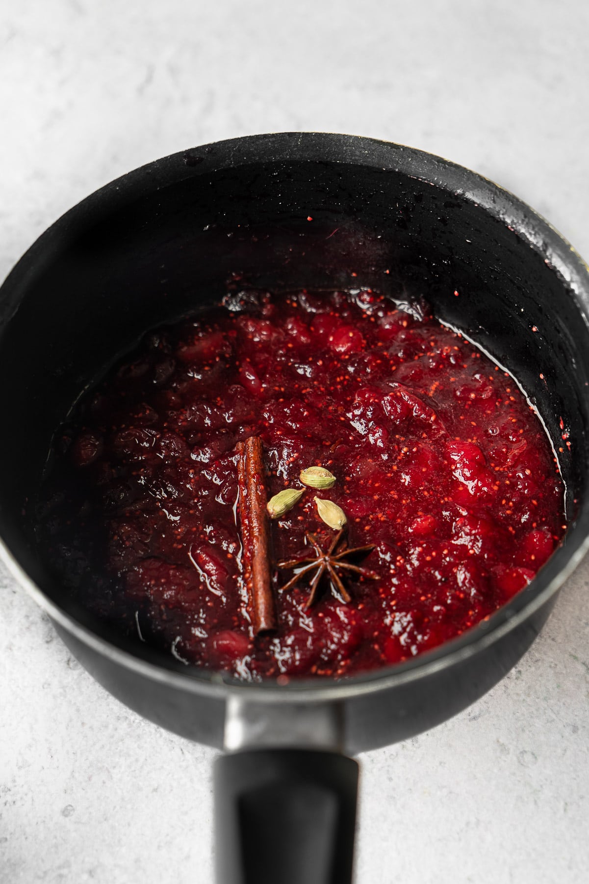 a sauce pot with cooked cranberry sauce with cinnamon, star anise, and cardamom pods