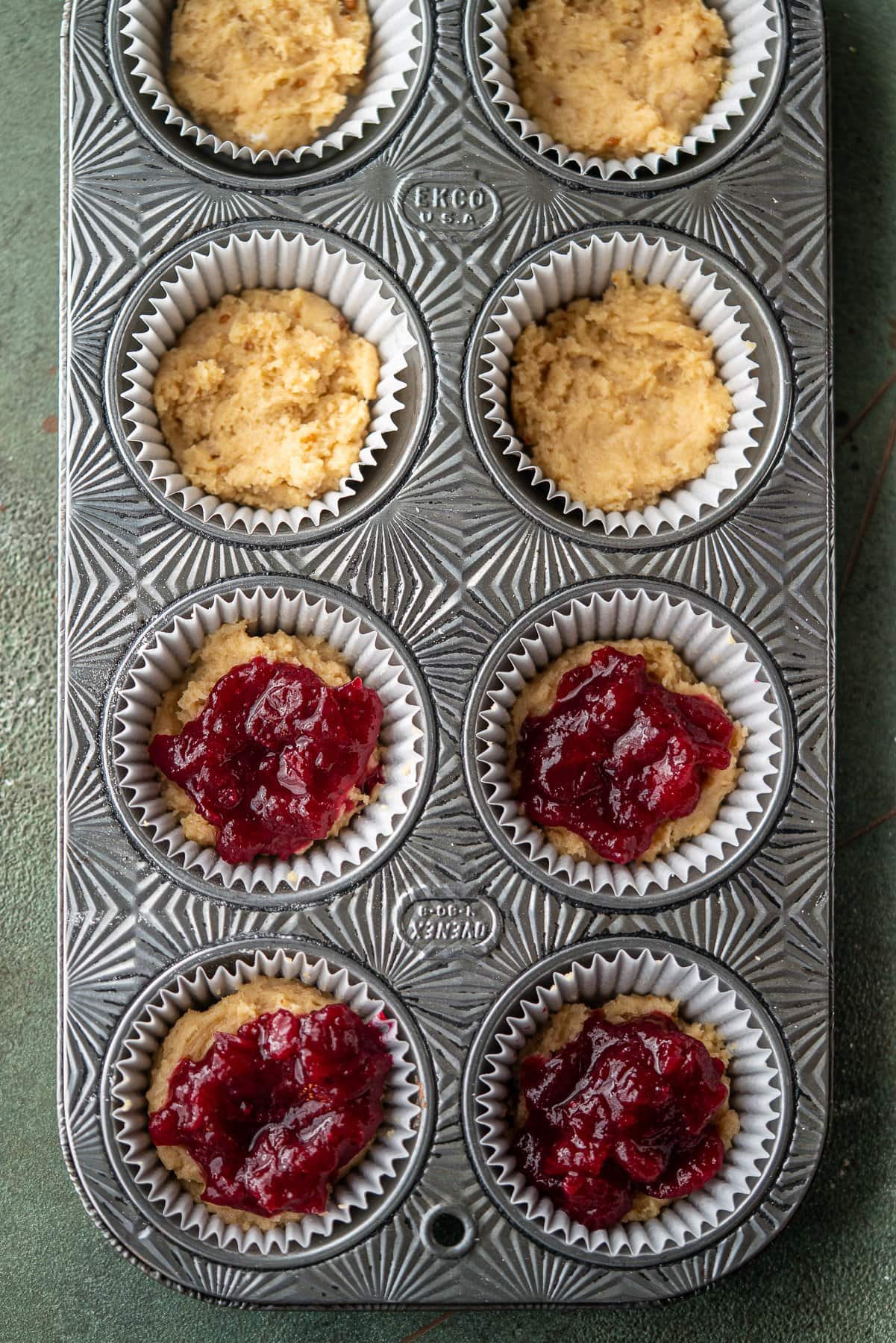 coffee cake muffin batter in a ovenex muffin pan with cranberry sauce in half
