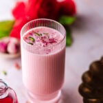 glass of rose lassi with roses in the background