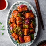platter with chili paneer surrounded by chopsticks, sauce, and sesame seeds